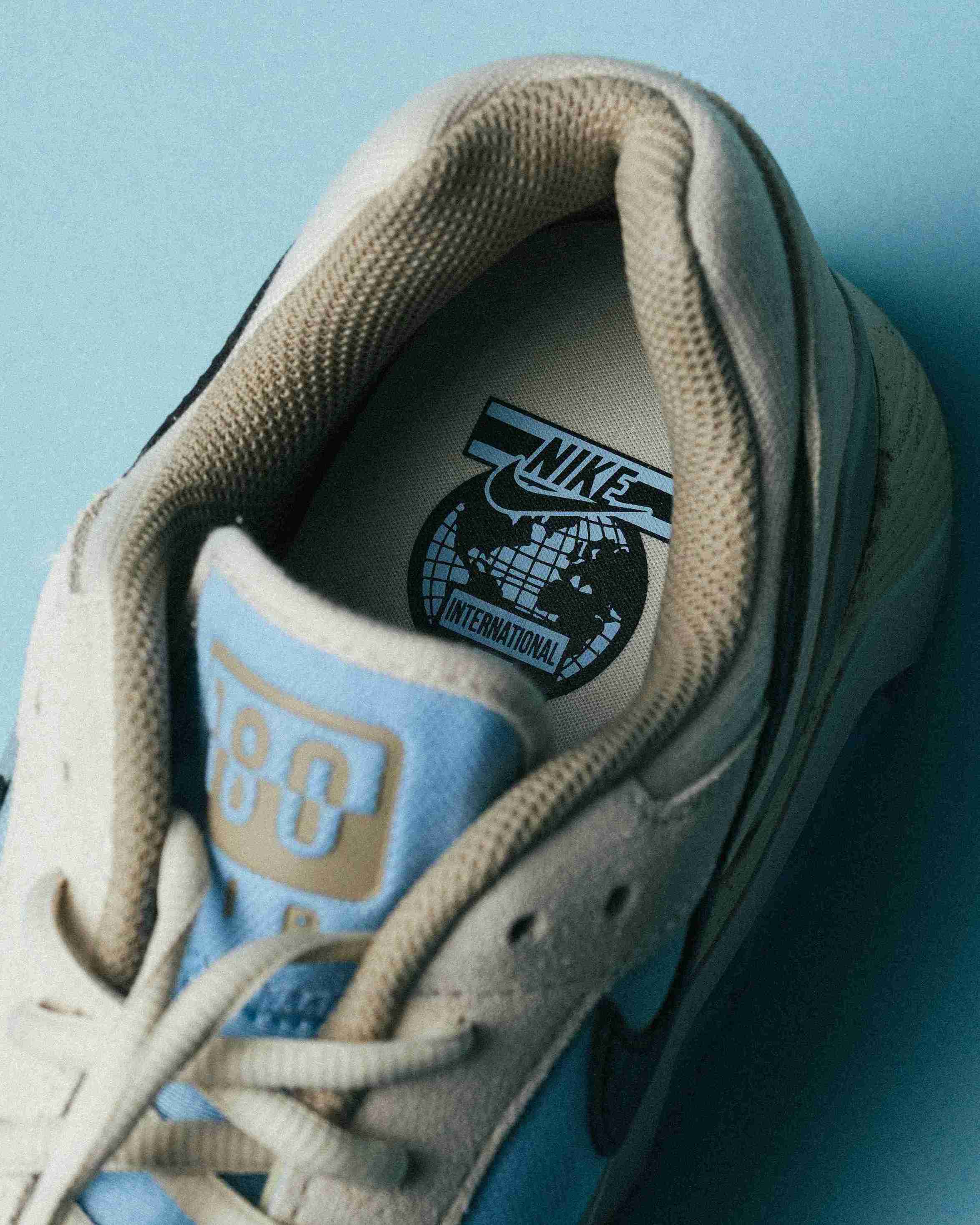 Paire de sneakers beige et bleu clair posée sur un fond bleu, vue de trois quarts avec mise en avant des formes et détails du modèle.